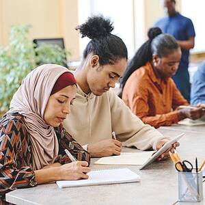 Drei Personen sitzen in einem Kurs und machen sich Notizen